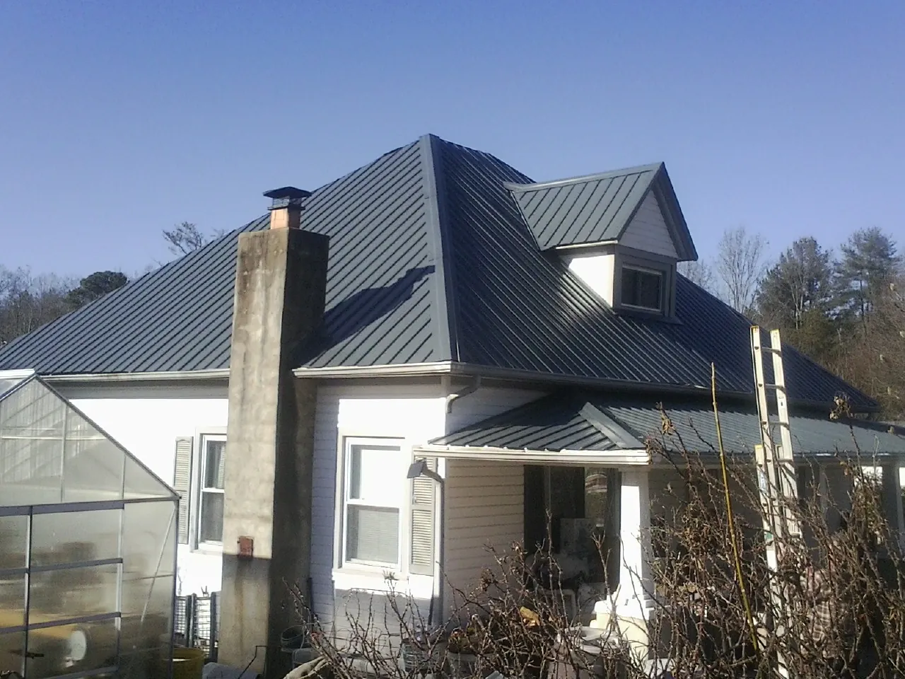 Dark blue standing seam metal roof on a white farmhouse with dormer — Slate & Tile Roof Repair by Roofing Brothers in South Greenfield