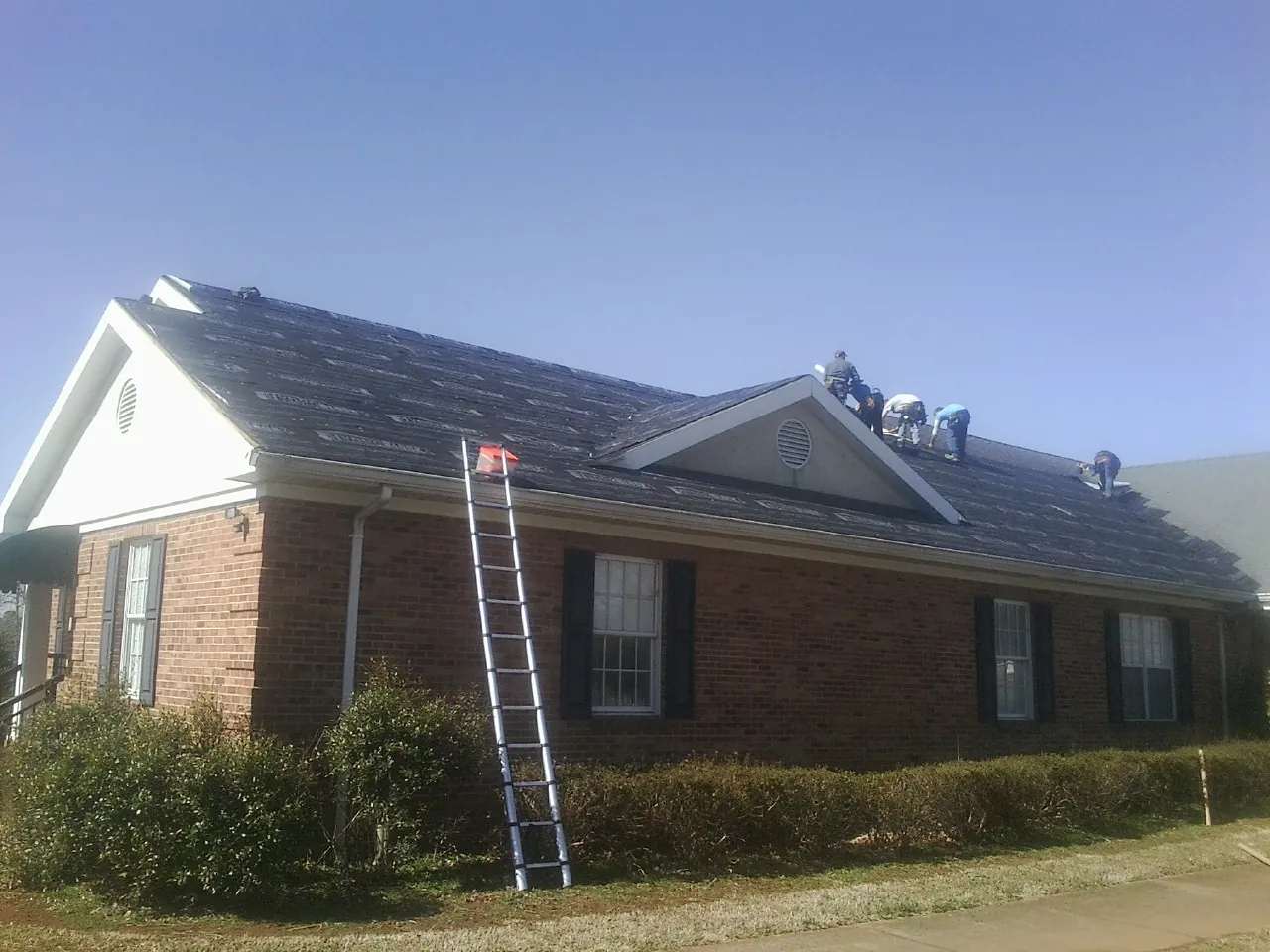 Crew tearing shingles off a brick ranch roof with a ladder set — Emergency Roof Repair work by our crew in South Greenfield