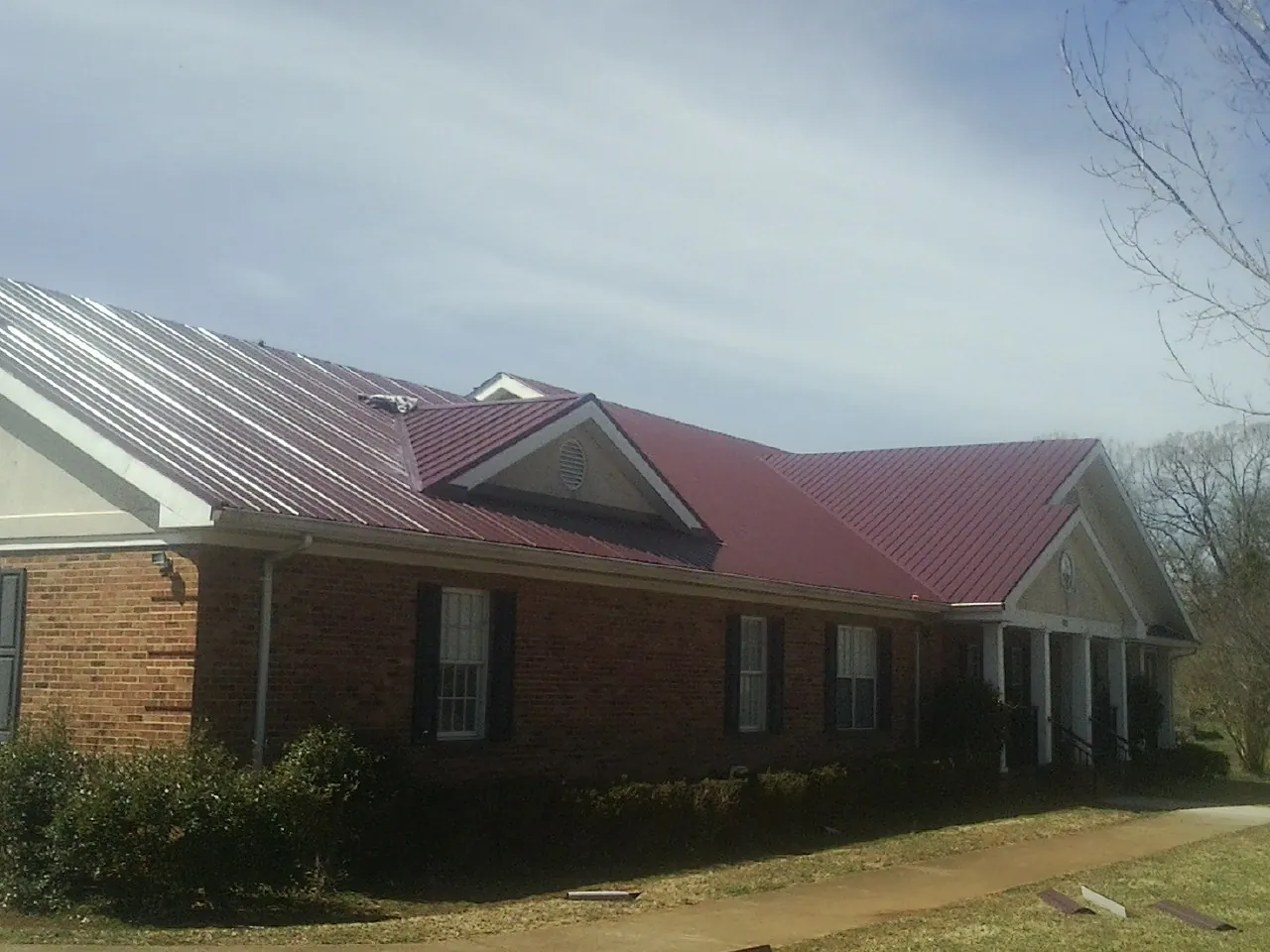 Red metal roof with gabled entries on a long brick building, from a Hail Damage Roof Repair job in South Greenfield