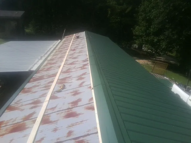 Old rusted panels beside newly installed green metal roofing — Wind Damage Roof Repair by Roofing Brothers in South Greenfield