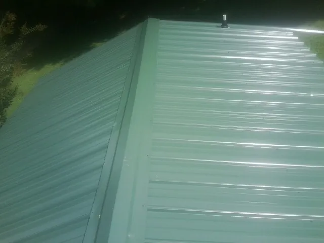 New green metal panels meeting at the ridge of a roof — Flat Roof Repair work by our crew in South Greenfield