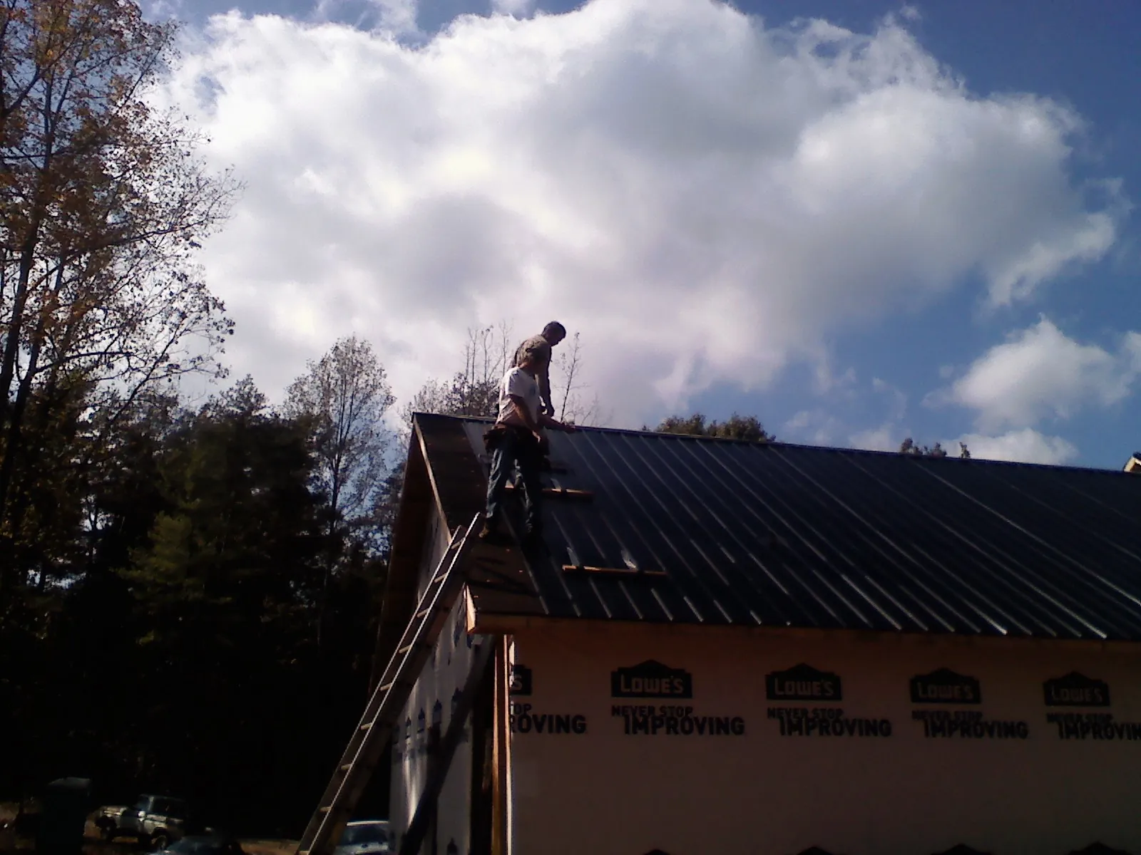 Roofer fastening dark metal panels high against a cloudy sky, from a Roof Inspection job in South Greenfield