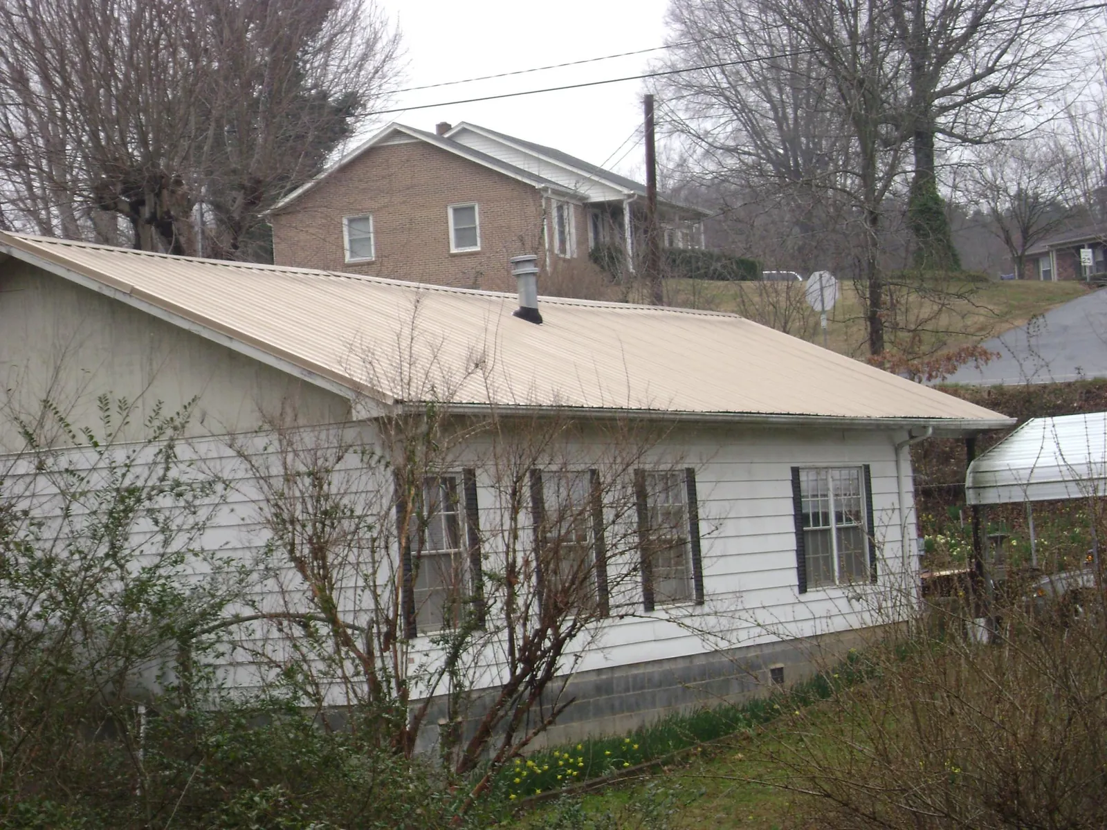 Tan metal roof on a white sided house set into a hillside — Commercial Roofing by Roofing Brothers in South Greenfield